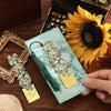 A vintage metal bookmark with an artistic hollow design and green tassel is held next to a bright yellow sunflower.