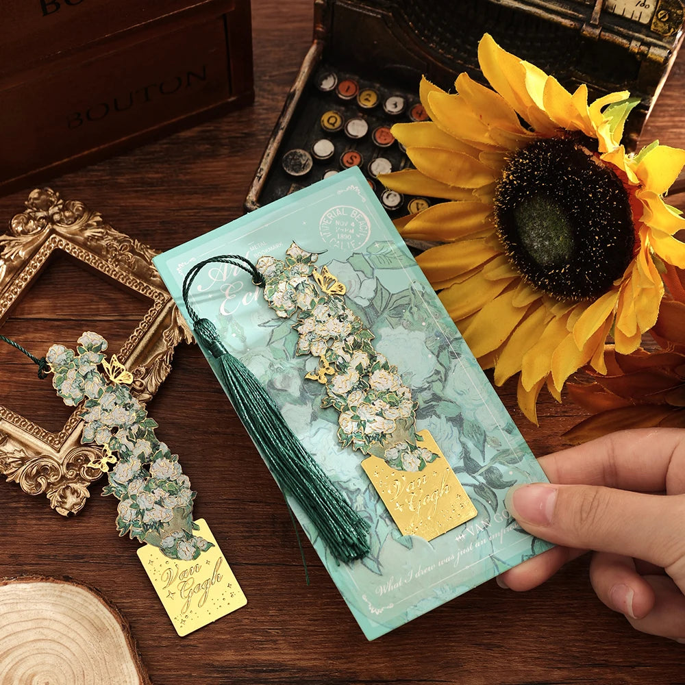 A vintage metal bookmark with an artistic hollow design and green tassel is held next to a bright yellow sunflower.