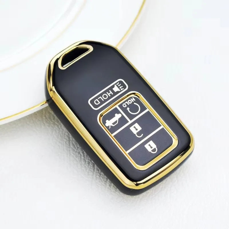 A black and gold TPU protective key case for a Honda vehicle is shown on a white surface.