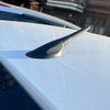 A close-up view of a black compact universal car radio antenna mounted on a white vehicle roof.
