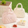 A pink quilted insulated lunch tote bag next to a cream-colored bag and fresh fruit on a white surface.