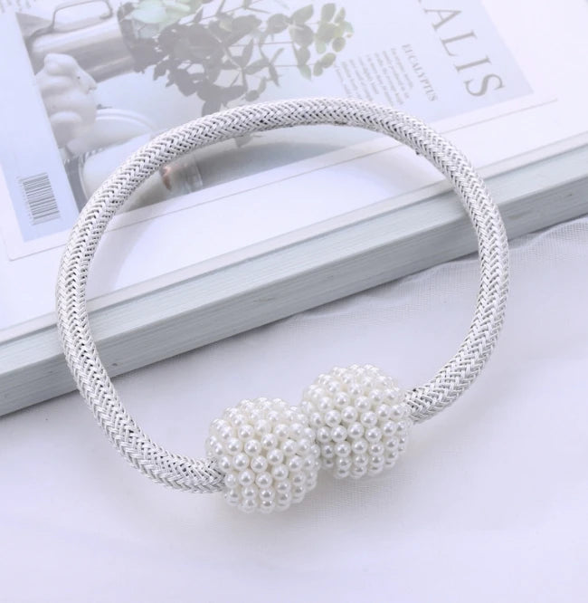 A silver-toned braided bracelet with a cluster of white pearls displayed on a book.