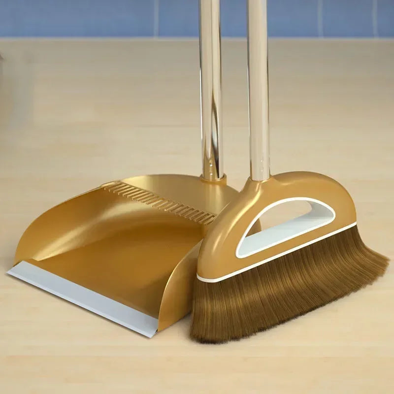 A gold broom and dustpan set with a floor wiper resting on a wooden surface.