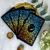 A black oracle card featuring a vibrant blue and gold floral design with a heart symbol on a white background.