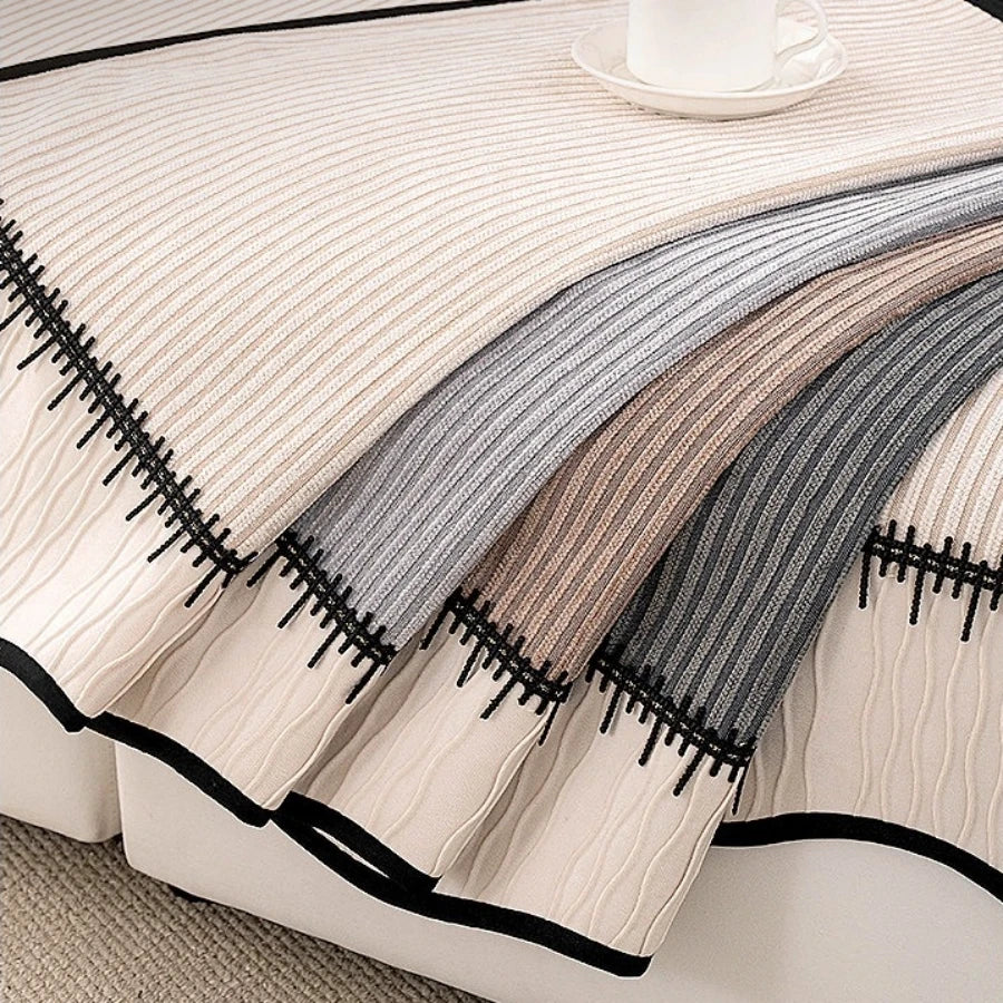 A close-up of a striped chenille sofa cover with pleated hems in beige, gray, and brown tones.