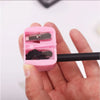 A pink automatic dual-hole pencil sharpener is held in a hand, showing the mechanism for sharpening pencils.