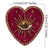 A deep magenta heart-shaped fabric patch decorated with gold and clear rhinestones forming an eye design.