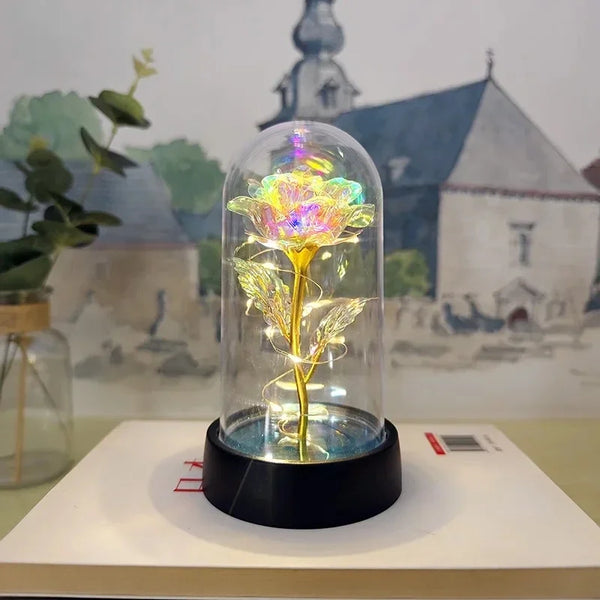 LED-Rosen-Nachtleuchte in Glas, leuchtet gelb und grün vor verschwommenen Gebäuden.