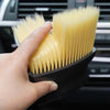 A hand holds a yellow car interior detailing brush set with soft bristles against a dark background.