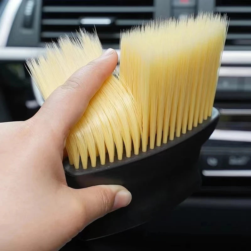A hand holds a yellow car interior detailing brush set with soft bristles against a dark background.