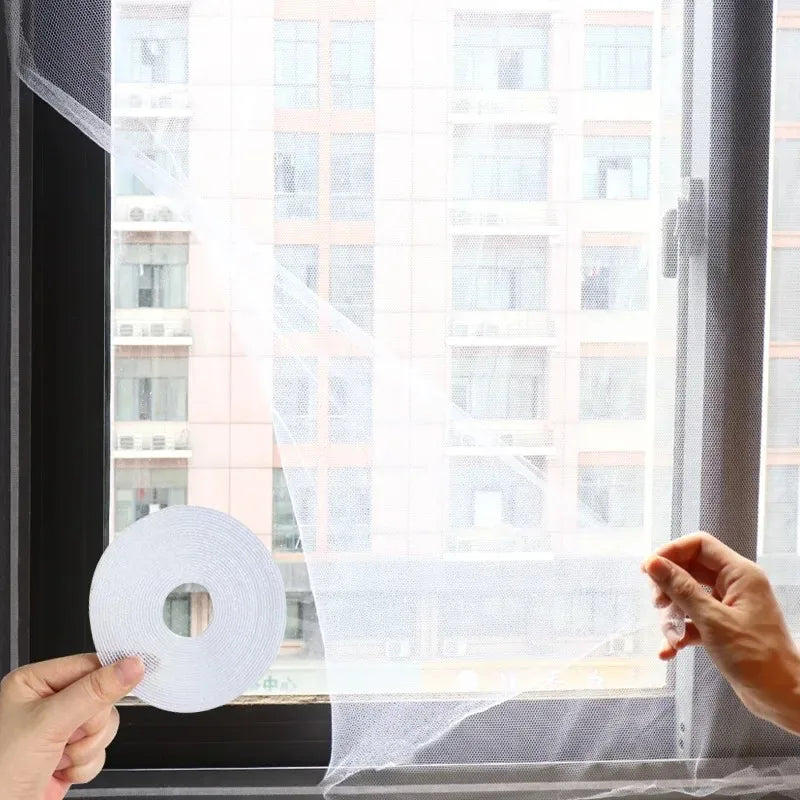 A hand is holding a roll of self-adhesive invisible mosquito screen material against a window.