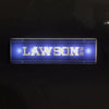 A rectangular blue light sign displaying the name LAWSON in gold lettering on a dark background.