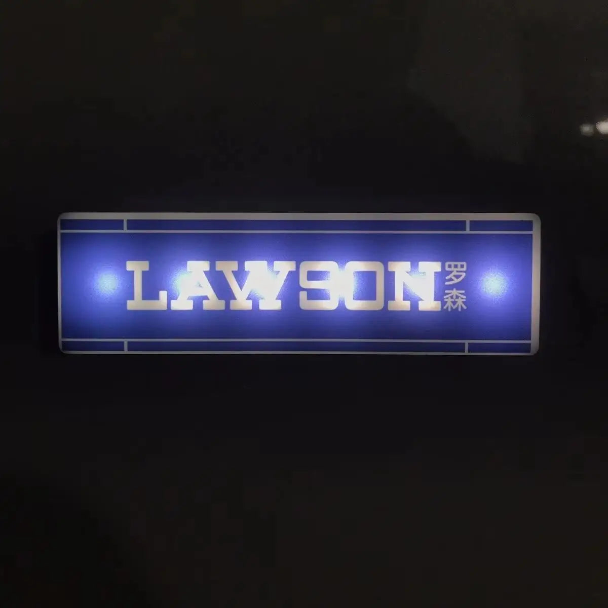 A rectangular blue light sign displaying the name LAWSON in gold lettering on a dark background.