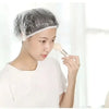 A person is applying a white product to their hair while wearing a disposable shower cap.