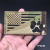 A rectangular tactical patch featuring a camouflage design with an American flag motif and paw print silhouette.