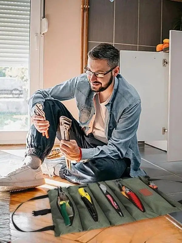 A man is organizing a roll-up multi-pocket tool organizer bag with various tools on a wooden table.
