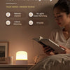 A woman is using a rechargeable touch and remote control RGB ambient lighting night light on a bedside table.