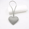 A heart-shaped gray PU leather keychain with a cotton peach charm resting on a white rolled surface.