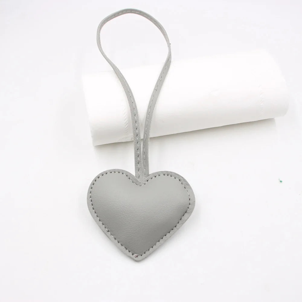A heart-shaped gray PU leather keychain with a cotton peach charm resting on a white rolled surface.