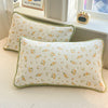 A close-up of a cream floral quilted pillow with a light green trim resting on a white surface.