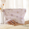 A light purple floral corduroy makeup bag with a secure zipper is being held by a hand.
