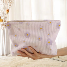 A light purple floral corduroy makeup bag with a secure zipper is being held by a hand.