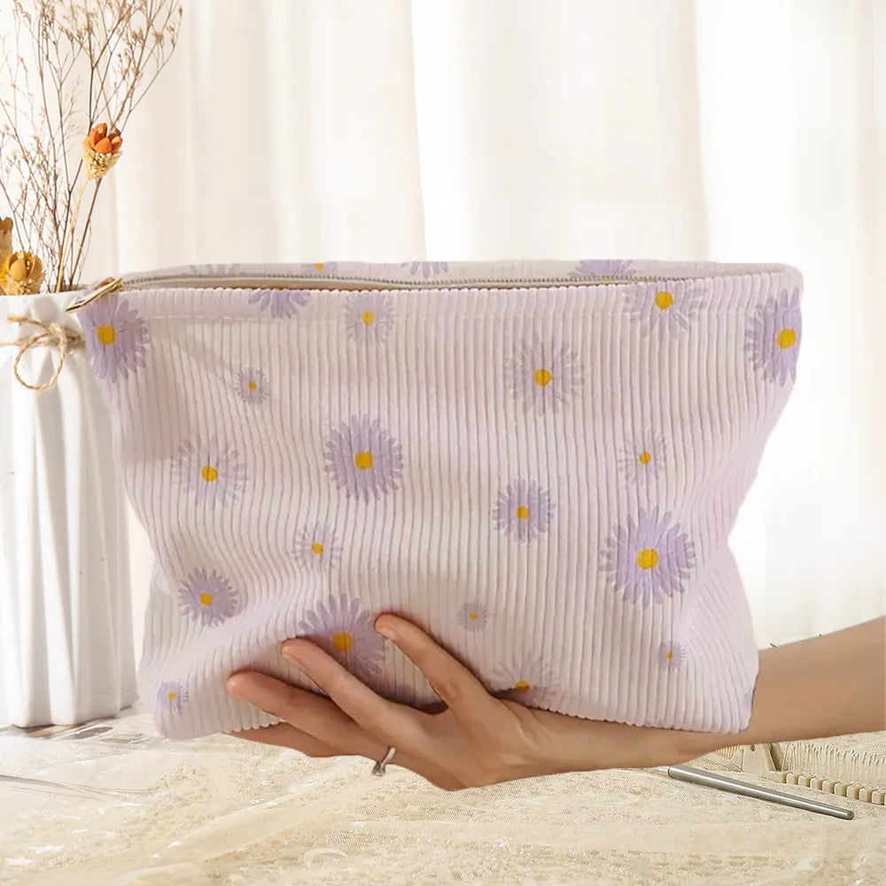 A light purple floral corduroy makeup bag with a secure zipper is being held by a hand.