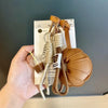 A hand holds a braided leather croissant keychain with a bag pendant and a gold chain.