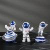 Three handcrafted astronaut figurines in white and blue resin on a black marble surface.