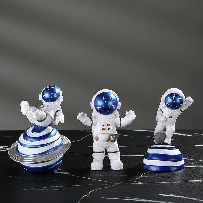 Three handcrafted astronaut figurines in white and blue resin on a black marble surface.