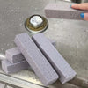 Several gray pumice stone cleaning sticks are displayed on a metal surface with a circular metal object.