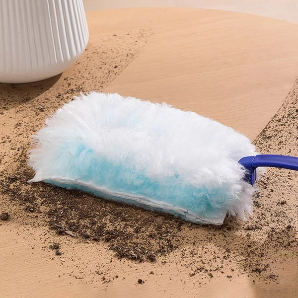 Un plumero electrostático azul y blanco peludo reposando sobre una superficie de madera clara con polvo esparcido.