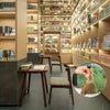 A hand holds a natural grass broom with a woven handle, positioned in front of a wooden desk.