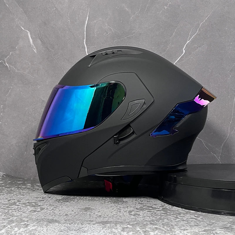 A black modular flip-up motorcycle helmet with a reflective blue visor resting on a gray surface.