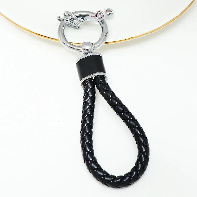 A black braided leather key fob cover with a silver split ring attached to a gold-colored cord.