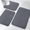 A set of gray plush memory foam bath mats with non-slip backing placed on a white tiled floor.