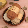 A basket filled with several rolls of natural colored cotton blend crochet yarn, including brown and beige shades.