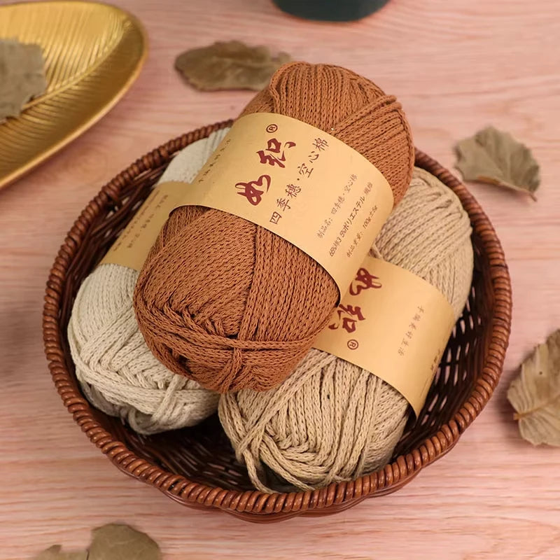 A basket filled with several rolls of natural colored cotton blend crochet yarn, including brown and beige shades.