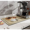 A silver coffee grinder and a natural fiber mat are displayed on a white countertop.