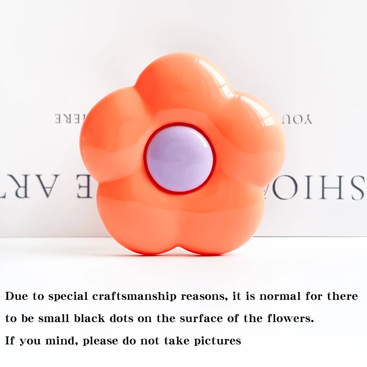 An orange flower-shaped silicone phone grip with a purple center and small black dots on the surface.