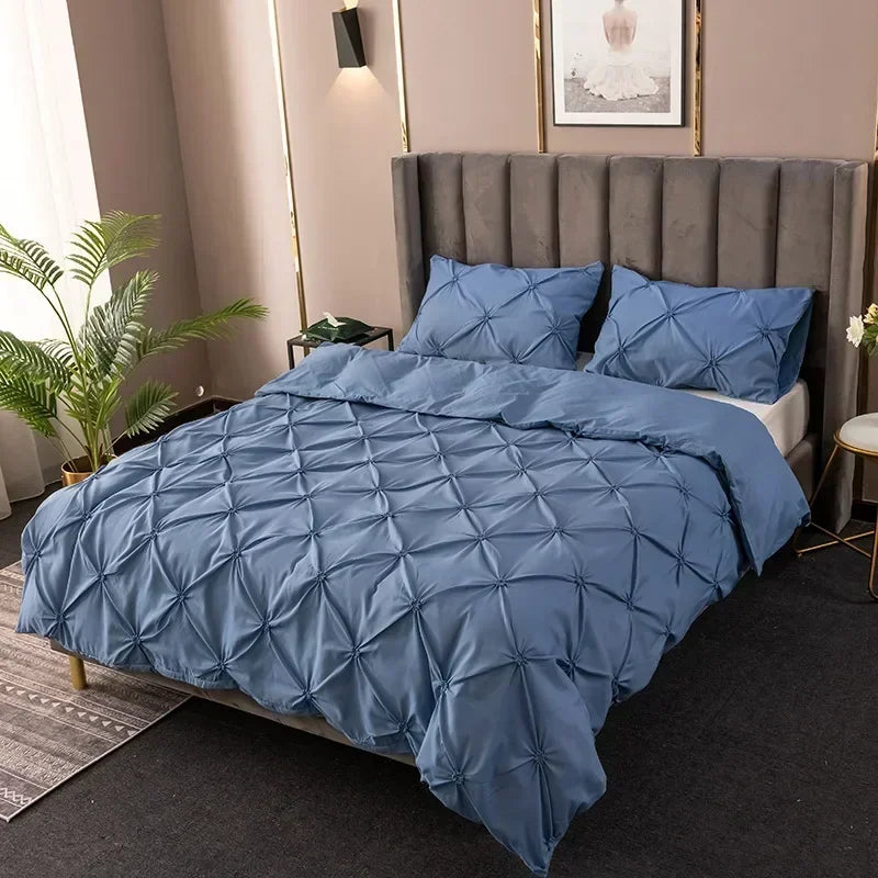 A blue pinch pleated duvet cover set displayed on a bed with a gray upholstered headboard.