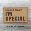 A rectangular tan patch with black text that reads Mama Says I'm Special on a wooden surface.