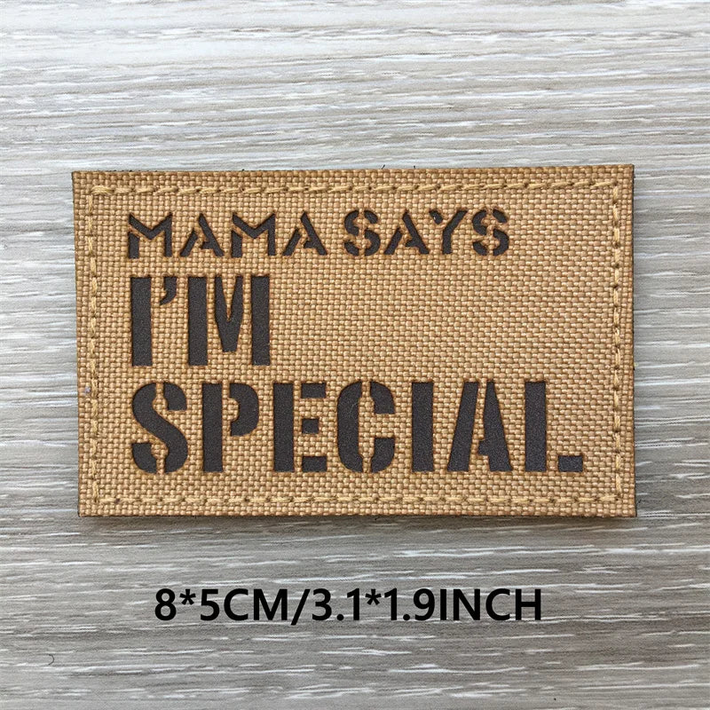 A rectangular tan patch with black text that reads Mama Says I'm Special on a wooden surface.