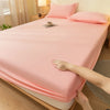 A pink fitted sheet is draped over a bed, showing the elastic edge and fabric texture.