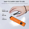 An orange multi-beam tactical flashlight is shown being carried on a hand with a wrist strap.
