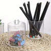 A clear acrylic jar holds a bundle of black cotton balls and swabs on a woven mat.