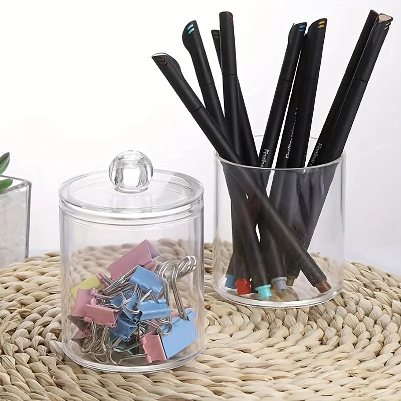A clear acrylic jar holds a bundle of black cotton balls and swabs on a woven mat.