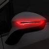 Close-up of a car mirror with bright red reflective safety strips illuminated.