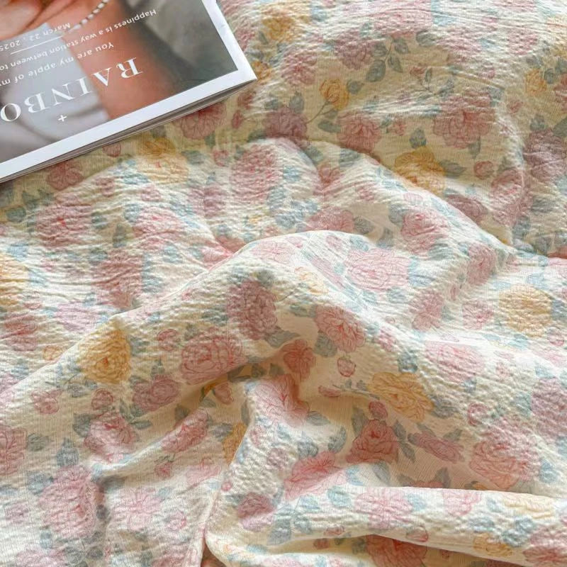 A soft pink and yellow floral washed cotton gauze summer quilt draped on a surface.