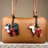 A tan leather handbag featuring a black and white Shiba Inu charm with a red braided bow.